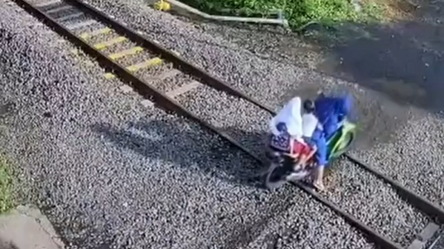 [動画0:28] 親子３人が乗るバイク、列車が近付く踏切で立ち往生